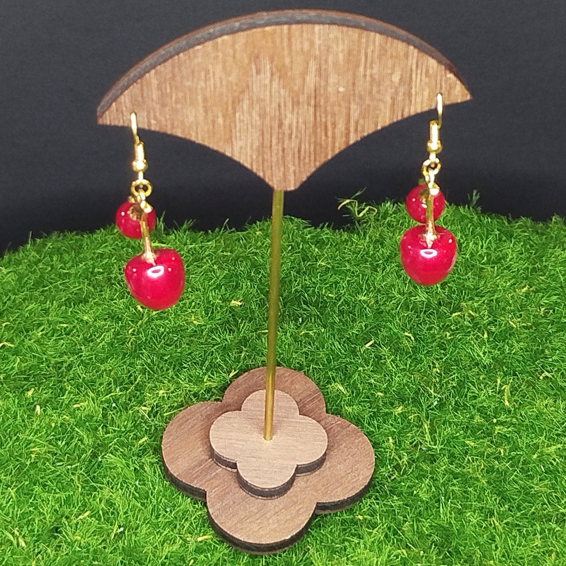 Red earrings on a wooden stand with a grass-like surface