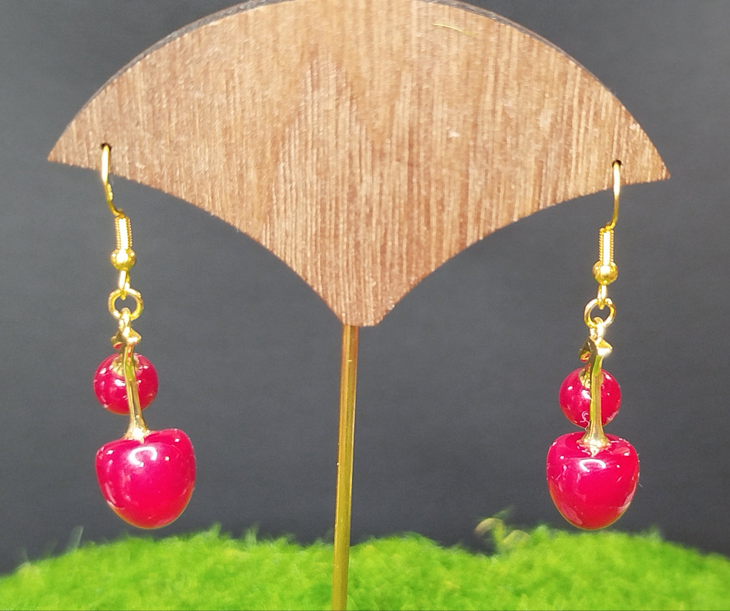 Pair of red cherry-themed earrings on a wooden stand with a dark background