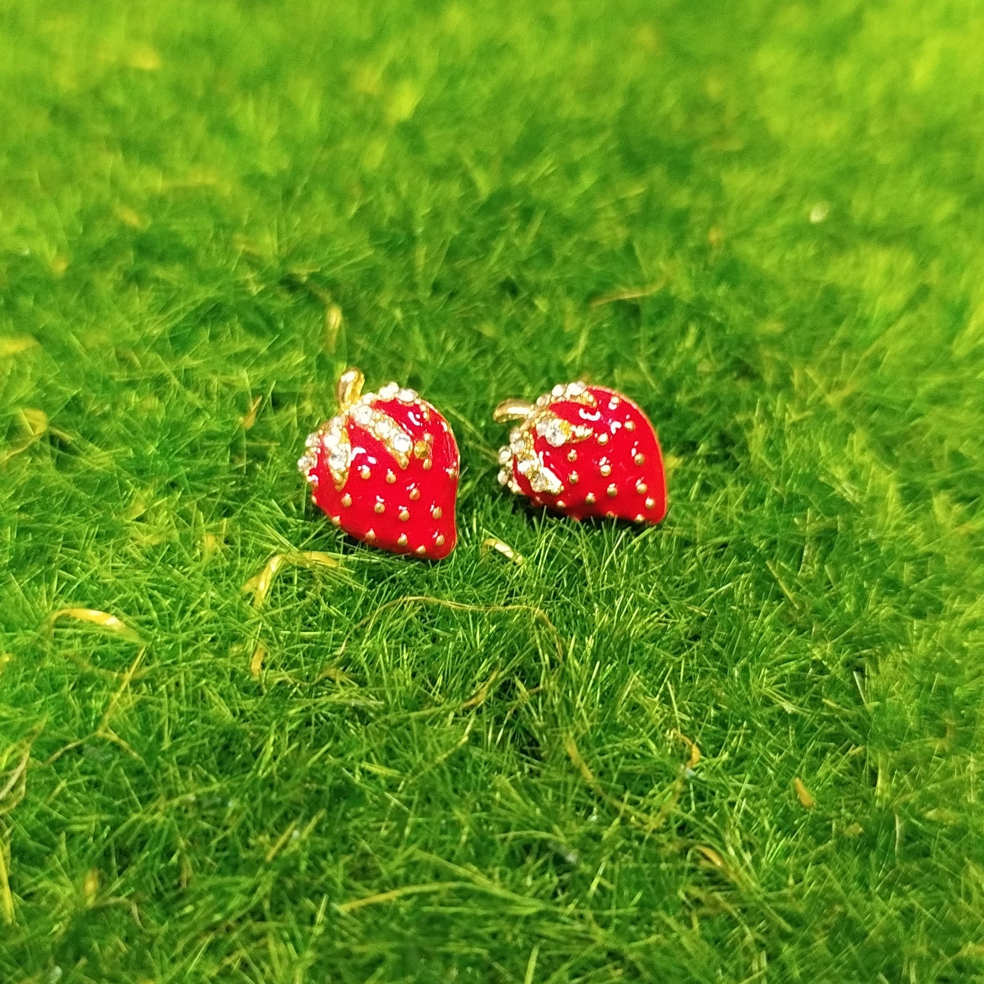 Red jordbær earrings on a green textured surface
