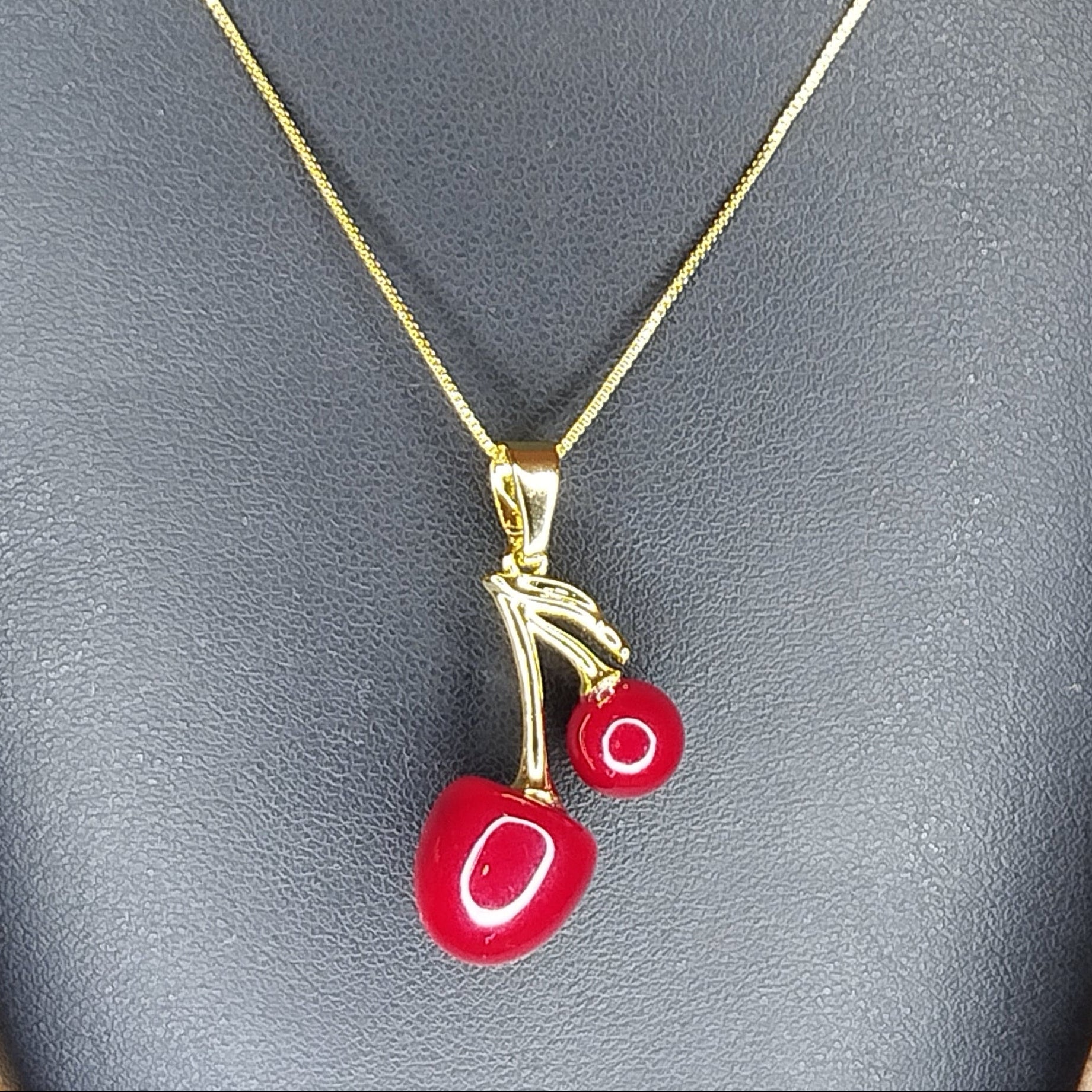 Gold necklace with cherry pendant on a black display stand