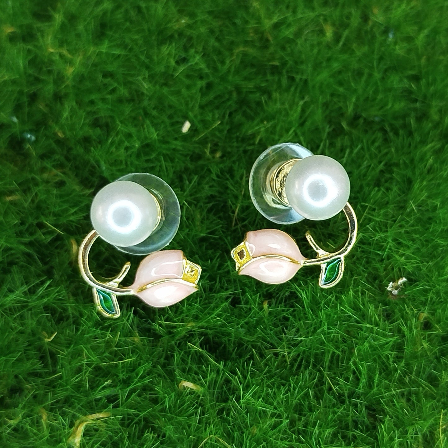 Pair of earrings with pearl-like beads and floral designs on a green grass background