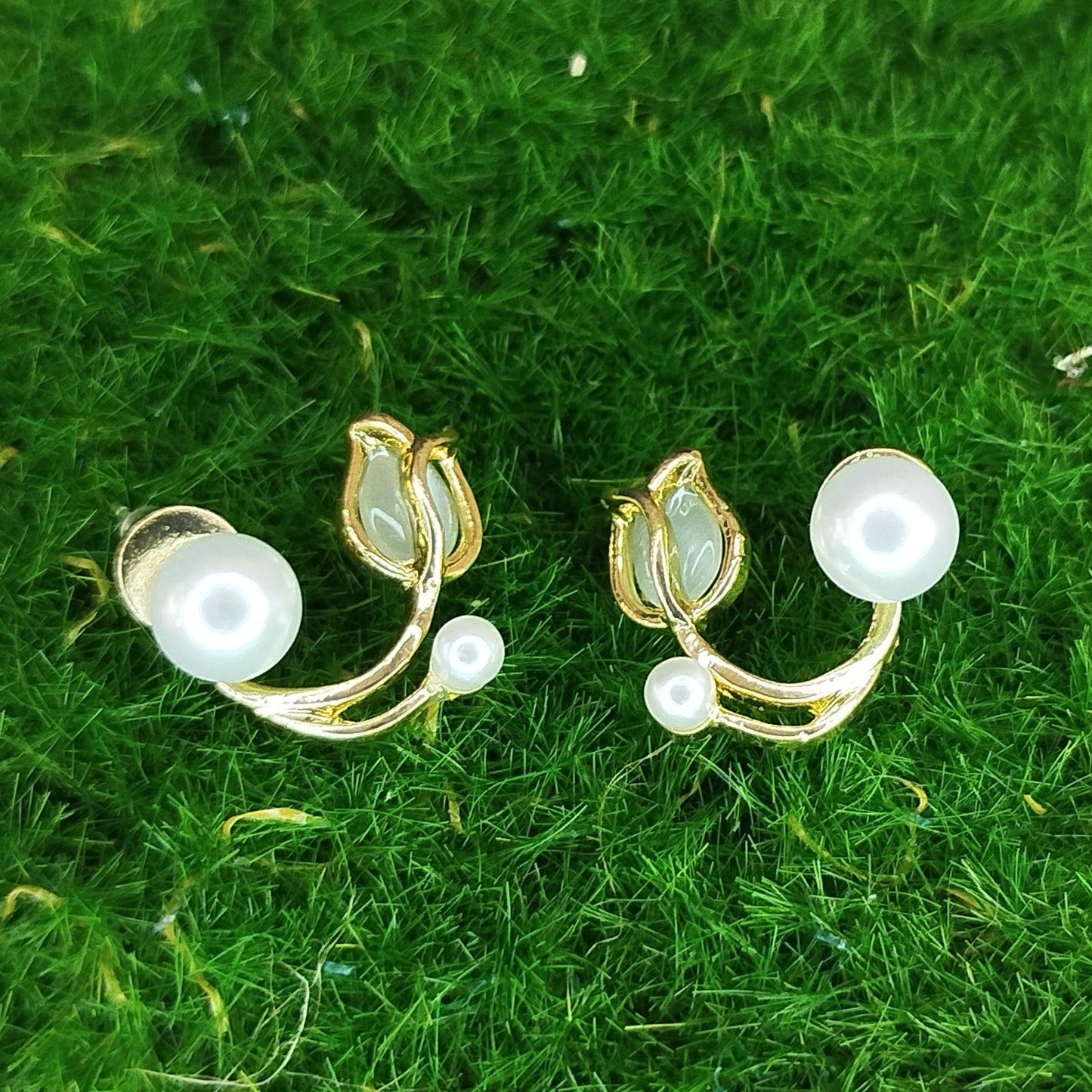 Pair of gold and pearl earrings on green grass
