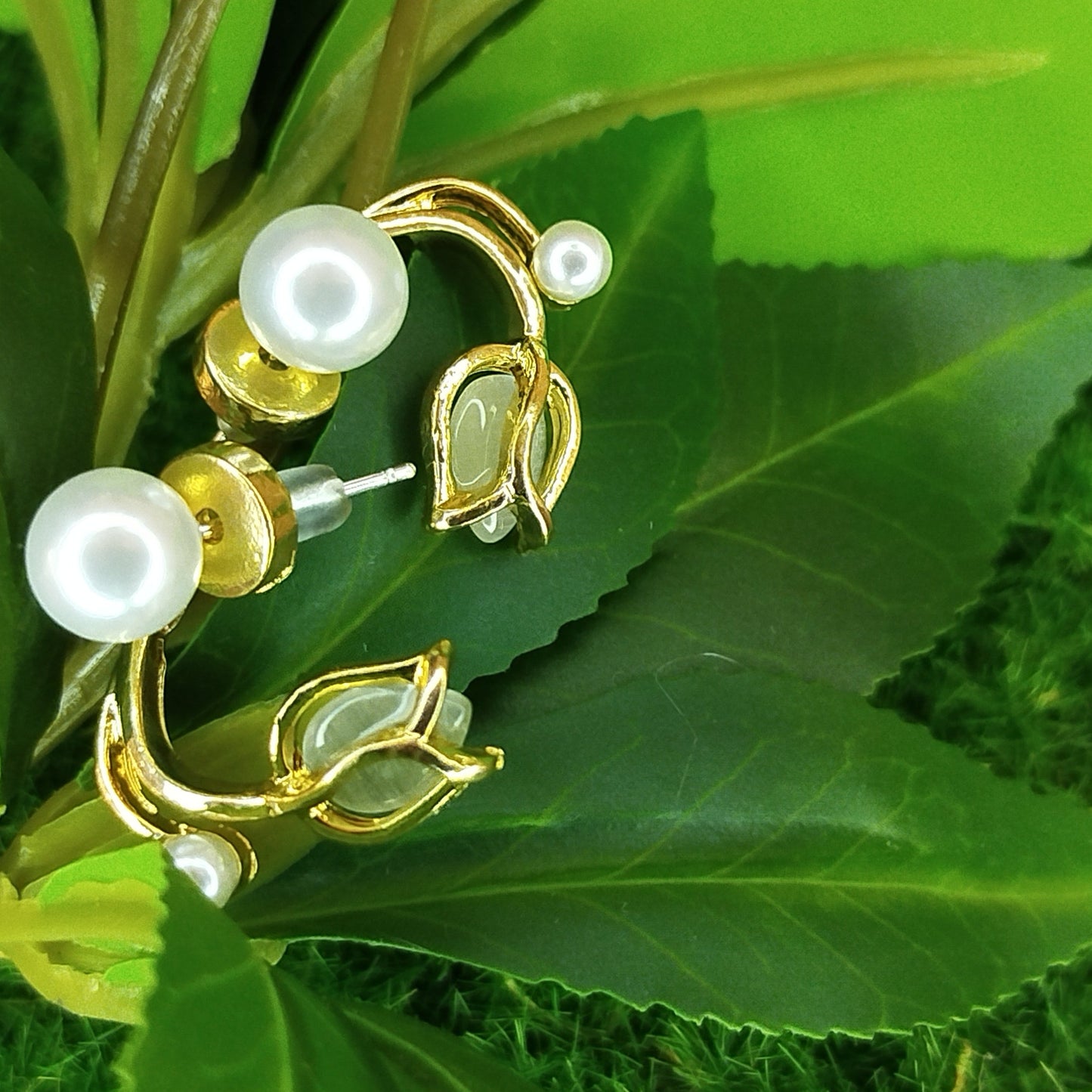 Gold and pearl earrings on green leaves