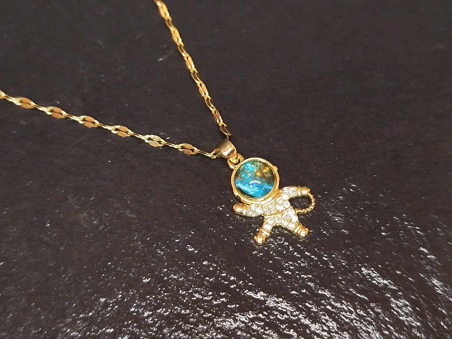 Gold necklace with a turquoise gemstone and small figure pendant