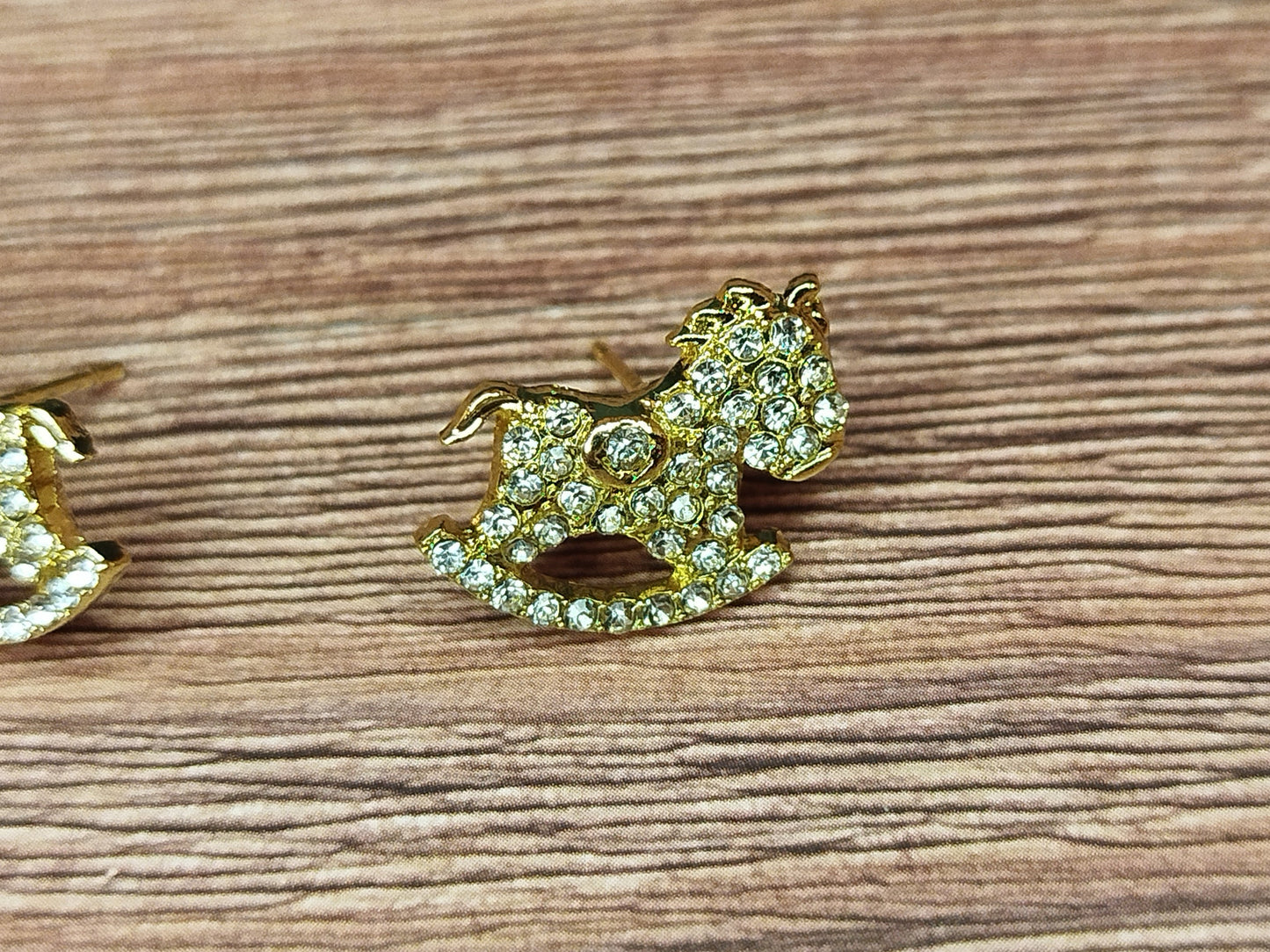 Gold horse-shaped earrings with gemstones on a wooden surface