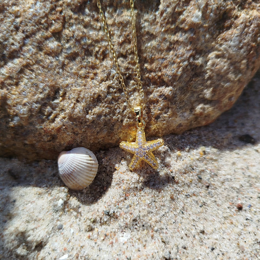 Gold starfish necklace on sand with a rock in the background
