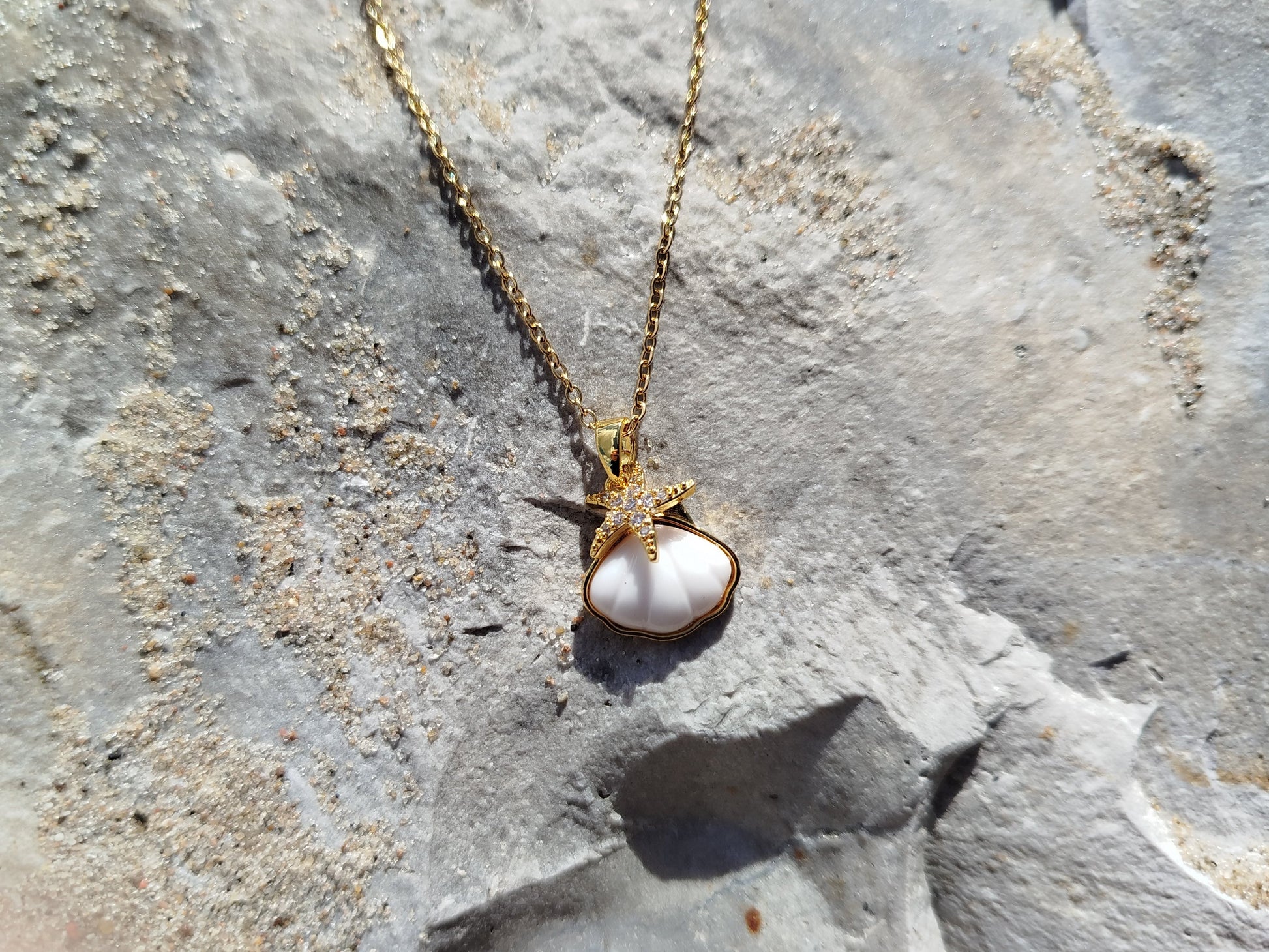 Gold necklace with a pearl pendant on a textured stone surface