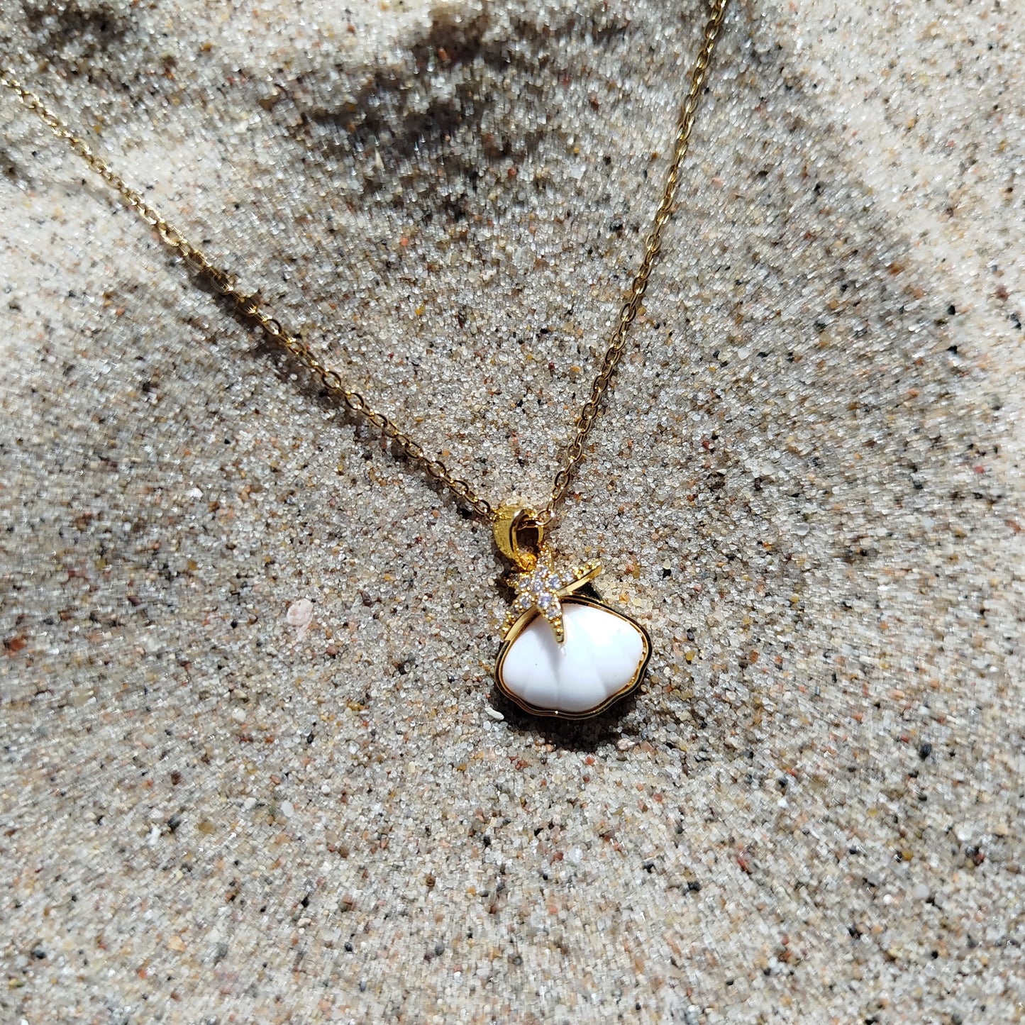 Gold necklace with a pendant on sandy surface