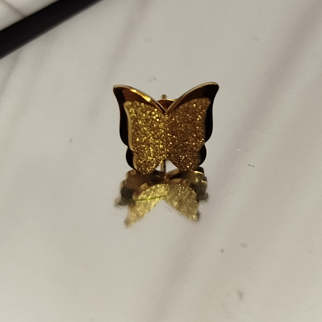 Gold butterfly-shaped earring on a reflective surface