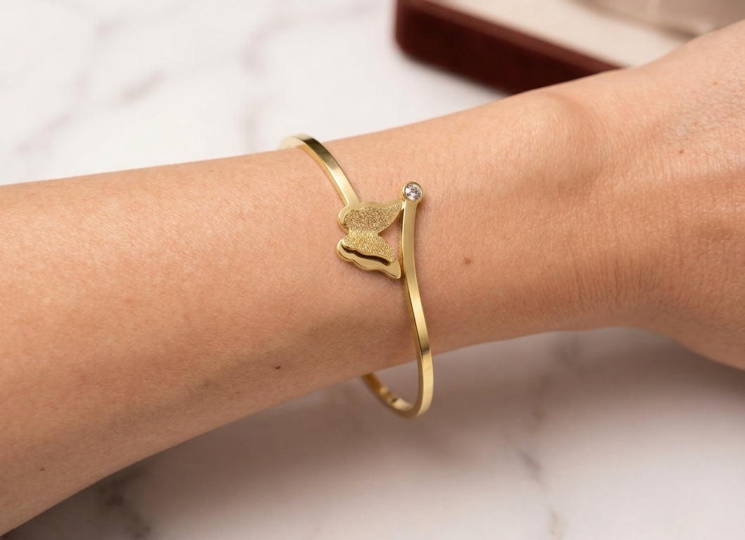Gold bracelet with a small gemstone on a wrist against a neutral background