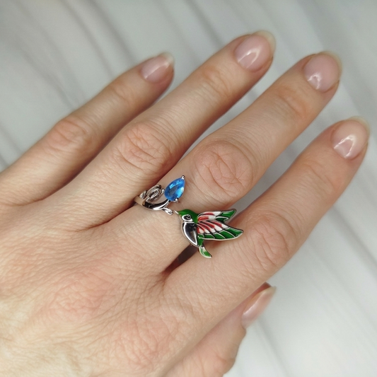 Hand wearing a decorative ring with a colorful bird design 